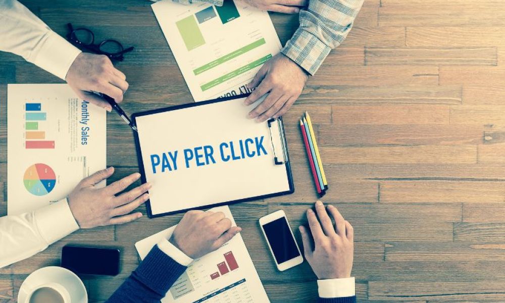 Team discussing pay-per-click strategy with reports and tablet on wooden table.