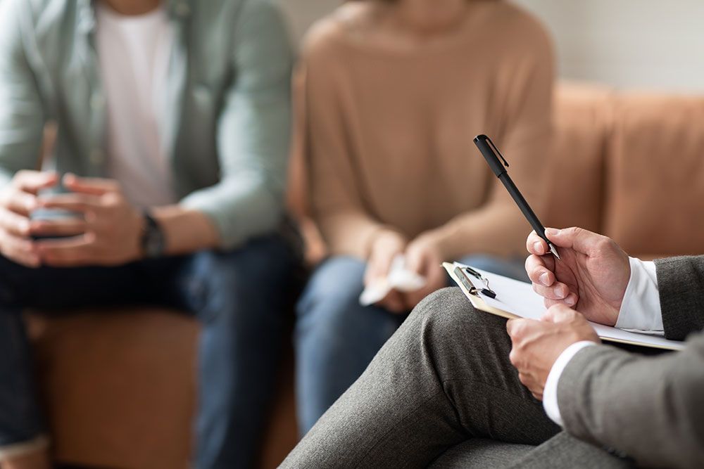 Therapist consulting couple during counseling session, taking notes on clipboard, close-up of hands and pen.