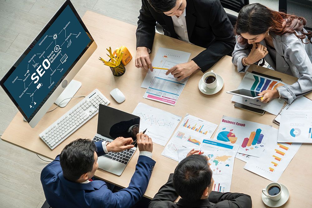 Team collaborating on SEO strategies with charts, graphs, and a computer screen displaying SEO concepts.