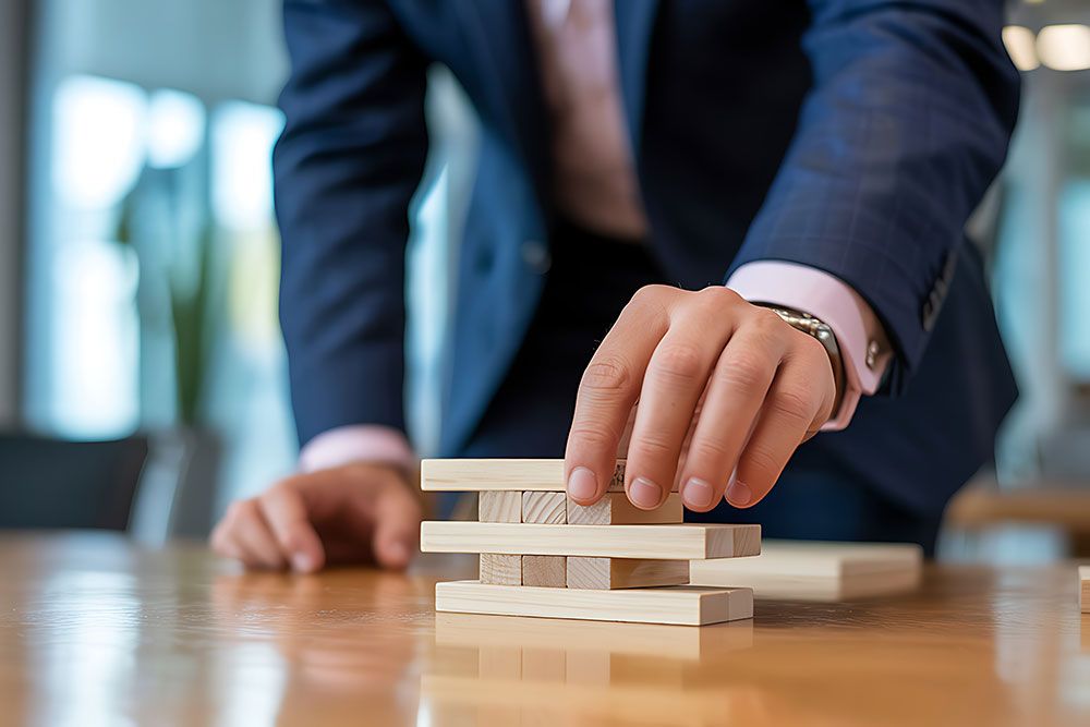 Business strategy concept: person in suit building structure with wooden blocks on an office table.