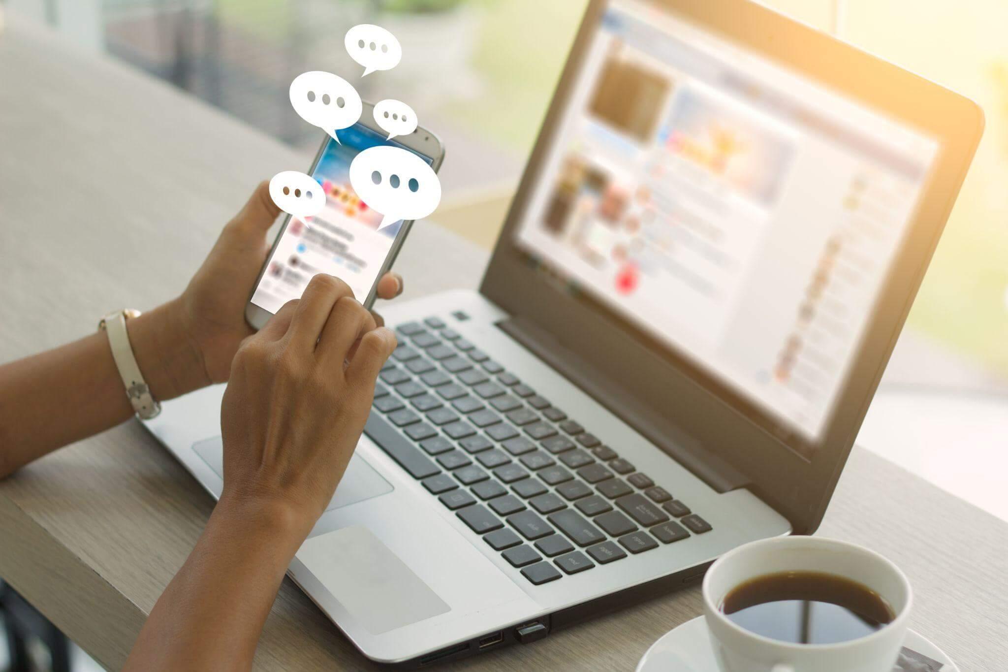 Person holding a cell phone in front of a laptop